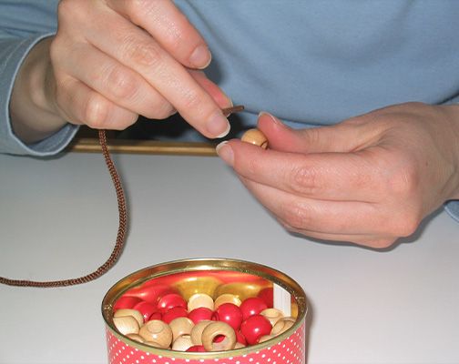 Eine Person fädelt Perlen in eine Dose und konzentriert sich auf die kreative Arbeit.